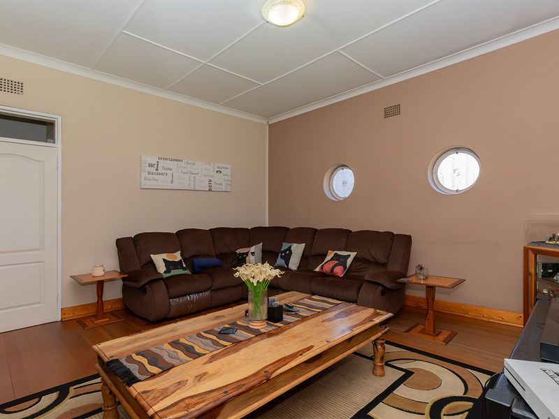 A living room featuring distinctive porthole windows, timber flooring, and traditional ceiling tiles, offering a unique architectural character ready for modern updates.