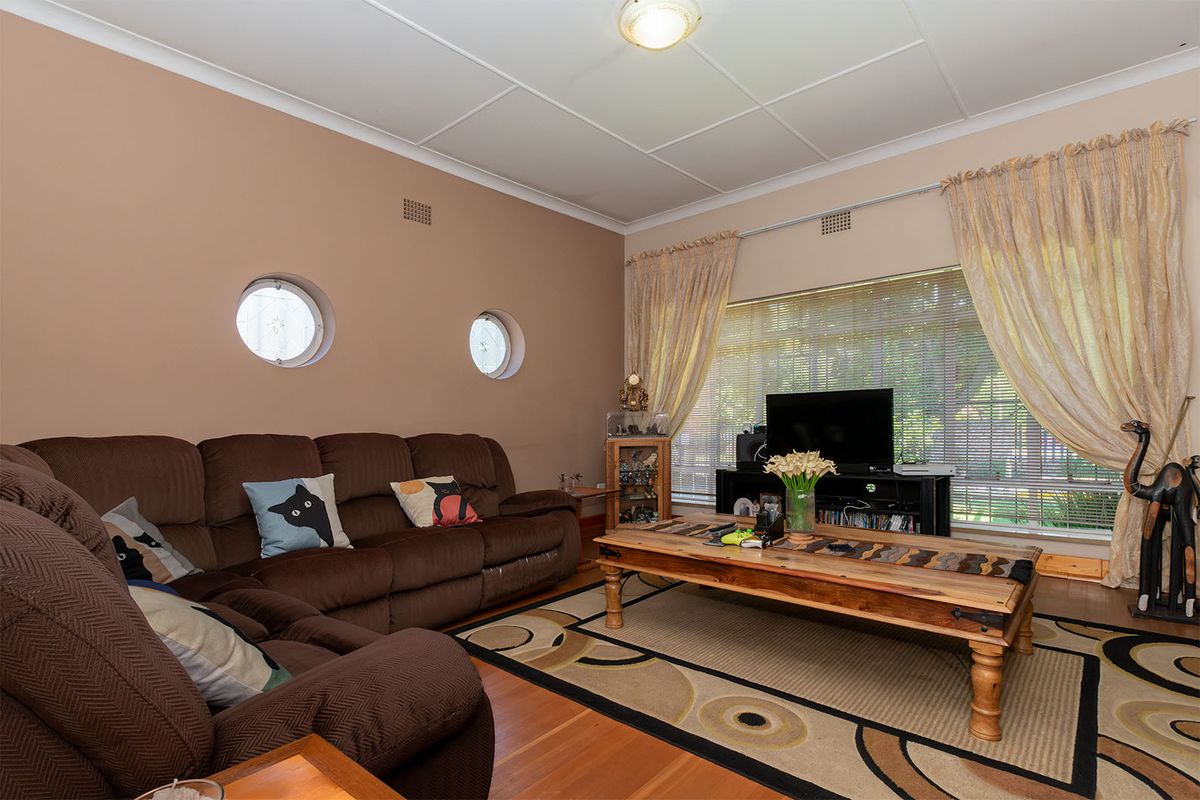 A comfortable living room featuring timber flooring, unique porthole windows, and a large window that allows for ample natural light.