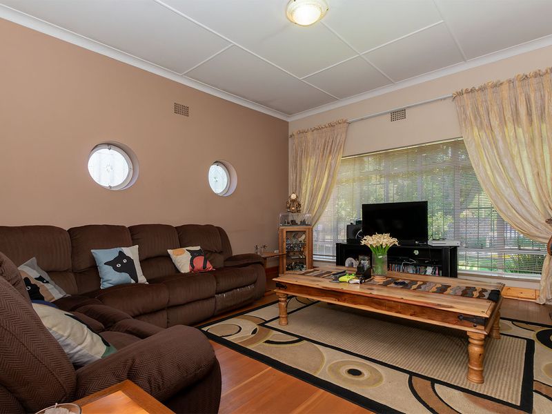 A comfortable living room featuring timber flooring, unique porthole windows, and a large window that allows for ample natural light.