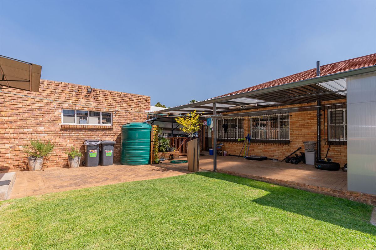 A rear exterior view featuring a paved patio area, covered outdoor space, brick facade, and a well-maintained lawn.