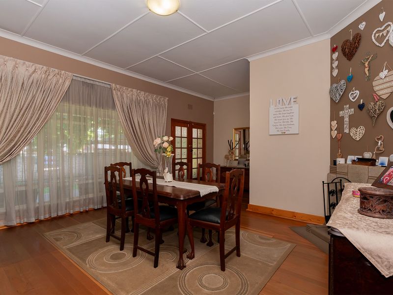 A dining room featuring timber flooring, a tiled ceiling, and a fireplace hearth, with large windows providing natural light.