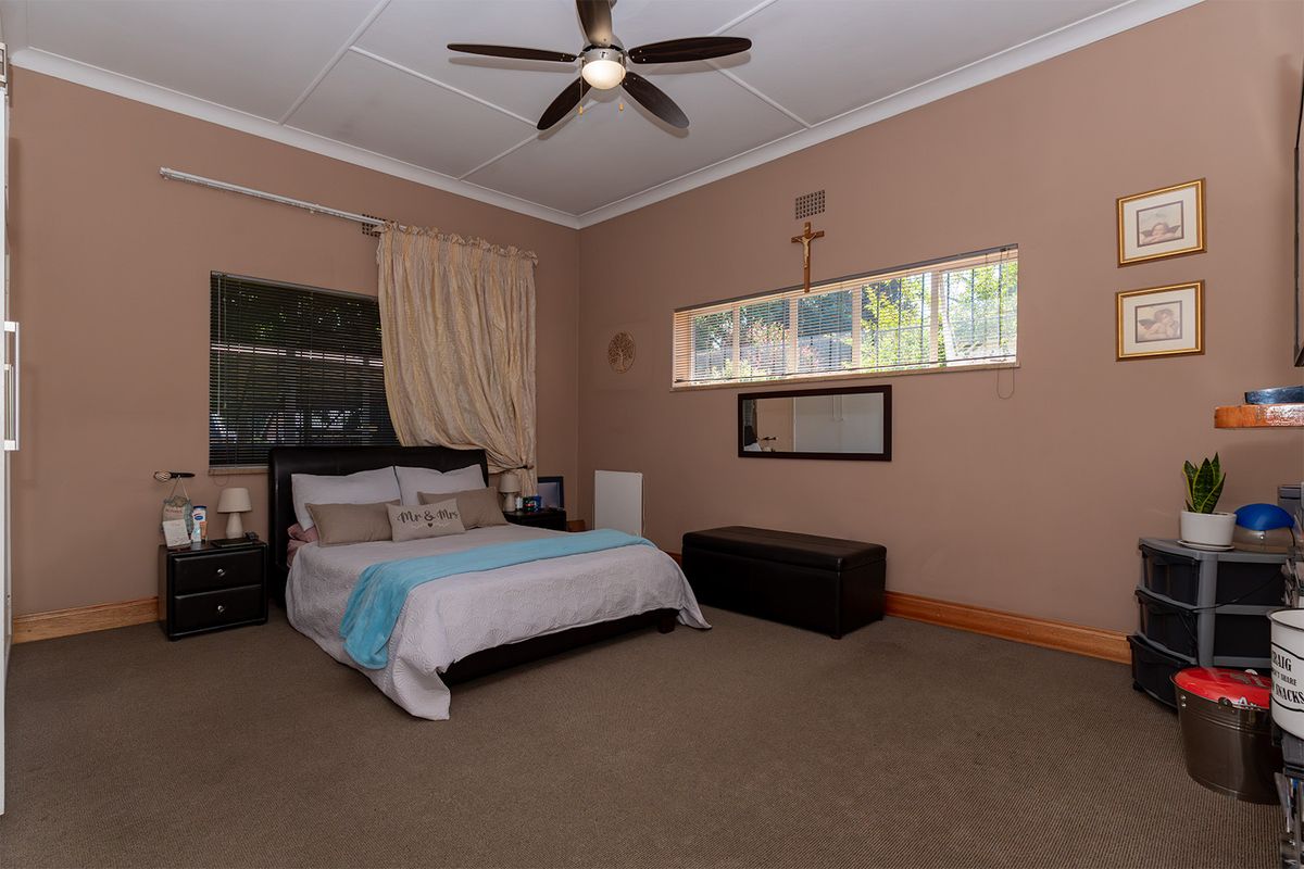 Spacious bedroom featuring neutral wall tones, carpeted flooring, ceiling fan, and natural light through horizontal blinds.