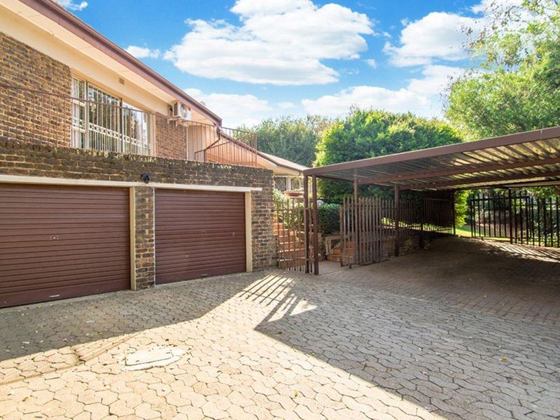 Front exterior view featuring a double garage, a spacious carport, and brick paved driveway area.