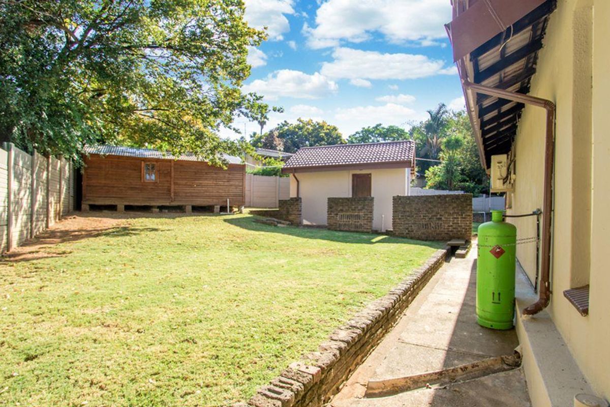 Rear garden area featuring a lawn, brick retaining wall, concrete pathway, and two separate outbuildings with a precast concrete boundary wall.
