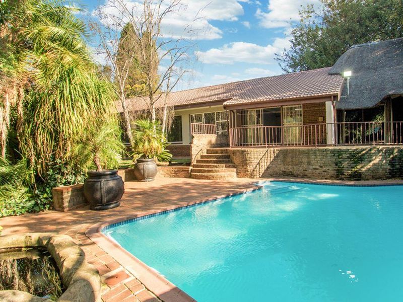 A spacious outdoor pool area featuring brick paving, a stone water feature, and a raised patio with metal railings, adjacent to the main residence.