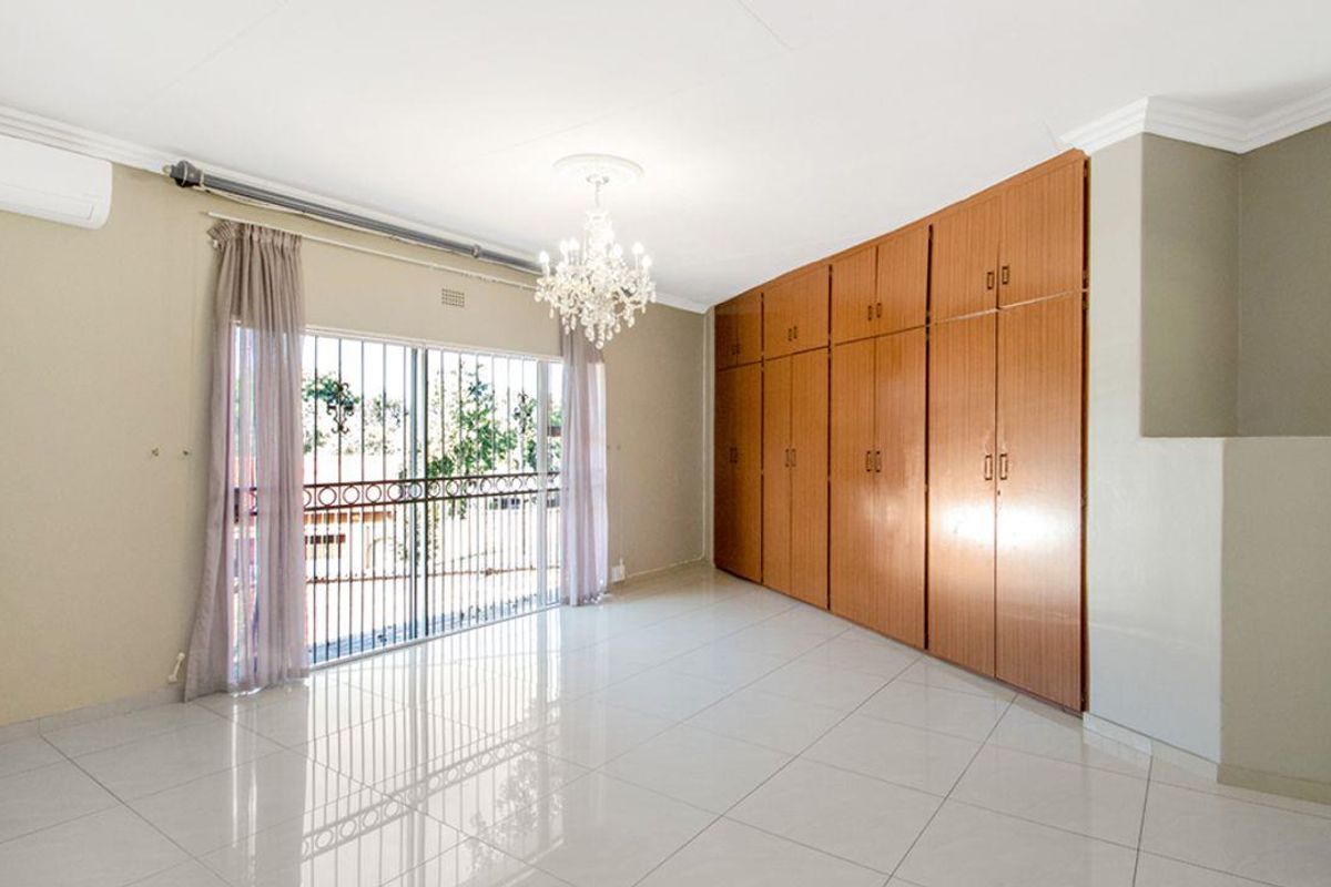 Spacious bedroom featuring large built-in wooden cupboards, polished tiled flooring, and a security gate leading to an outdoor area.
