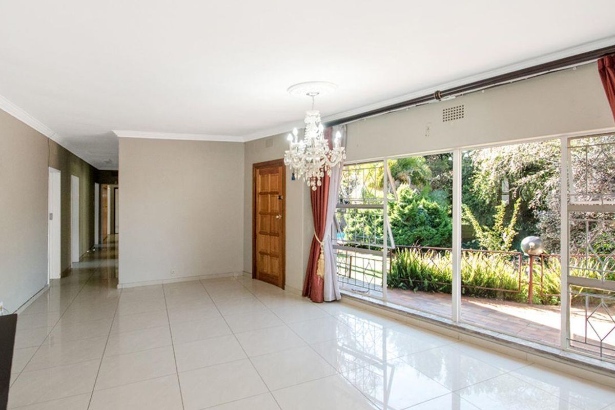 Spacious, light-filled living area featuring large sliding glass doors with security bars, tiled flooring, and a decorative ceiling rose.