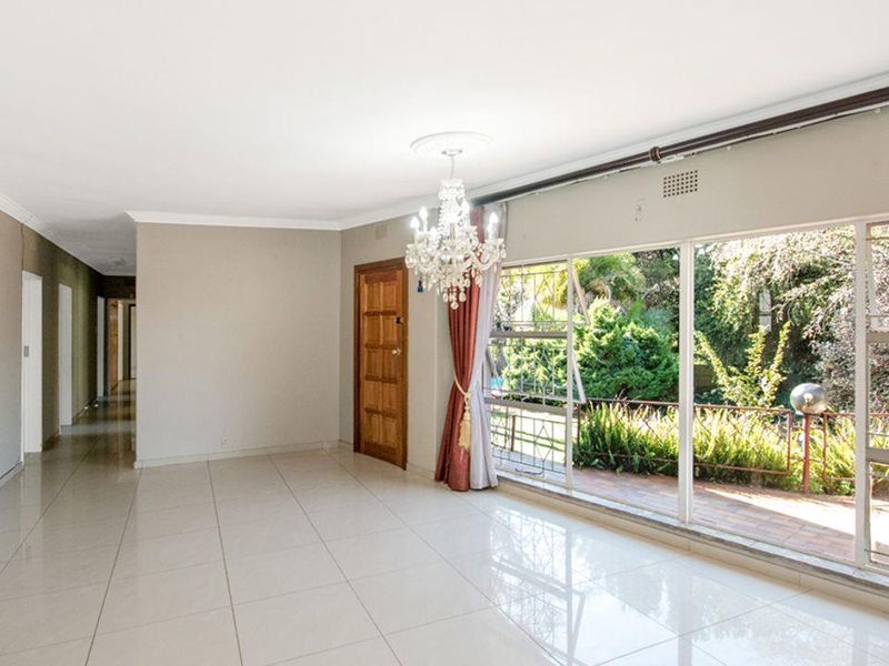 Spacious, light-filled living area featuring large sliding glass doors with security bars, tiled flooring, and a decorative ceiling rose.
