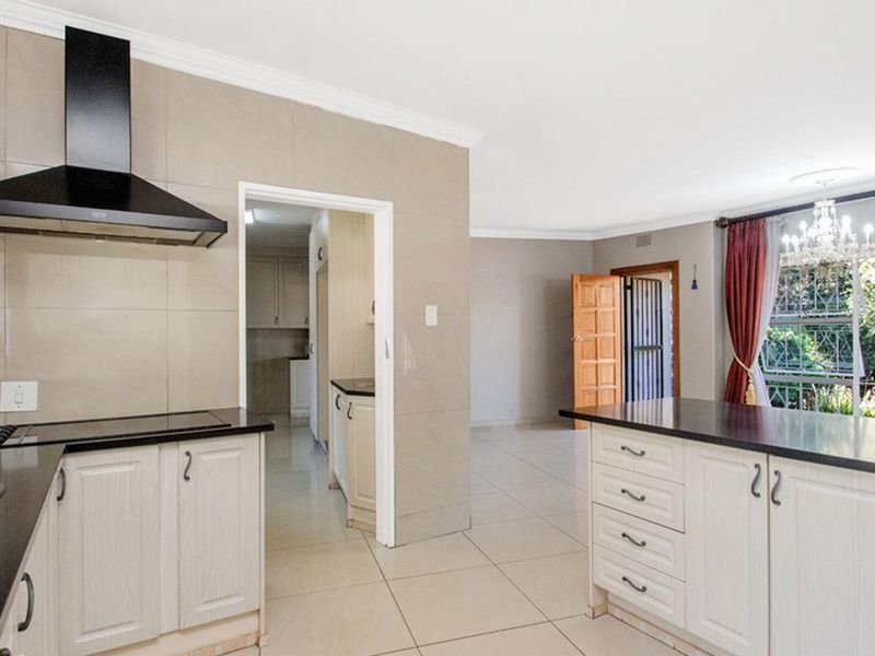 An open-plan kitchen featuring light-toned cabinetry, dark granite countertops, a modern extractor fan, and tiled flooring, flowing into an adjacent living area.