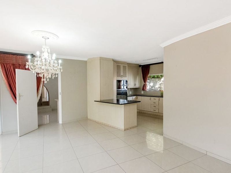 Spacious open-plan living and kitchen area featuring neutral ceramic tiling, built-in cabinetry with granite countertops, and an elegant central chandelier.