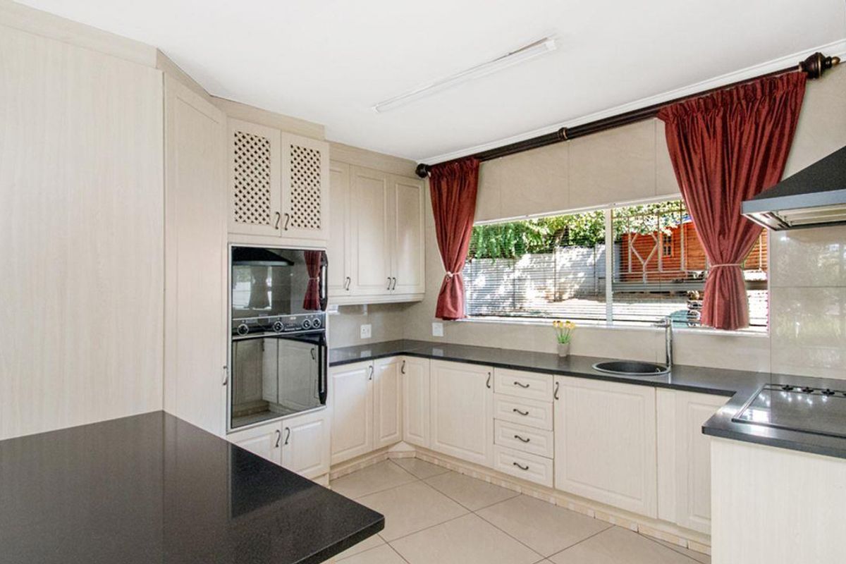 A functional kitchen featuring light-toned cabinetry, dark granite countertops, built-in oven, hob, extractor fan, and tiled flooring with a view of the garden.