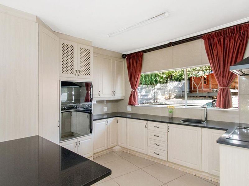 A functional kitchen featuring light-toned cabinetry, dark granite countertops, built-in oven, hob, extractor fan, and tiled flooring with a view of the garden.
