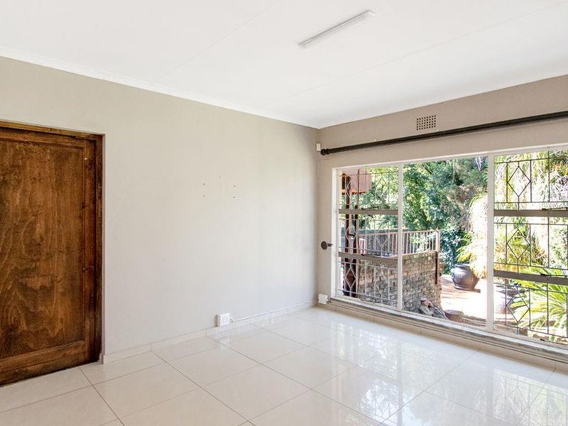 A bright, empty living room featuring large windows with security bars, tiled flooring, and a wooden door leading to the exterior.