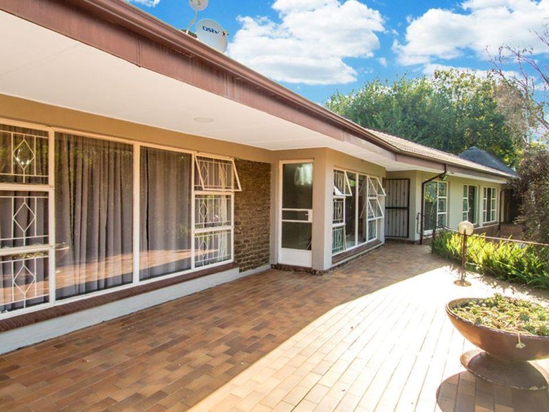 A spacious paved patio area featuring large windows with security bars, providing a functional outdoor space connected to the main house structure.