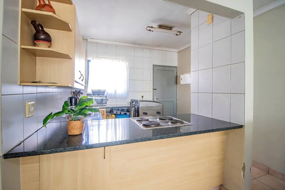 A functional kitchen featuring light wood cabinetry, granite countertops, an integrated electric hob, and tiled splashbacks, offering a practical layout for daily use.