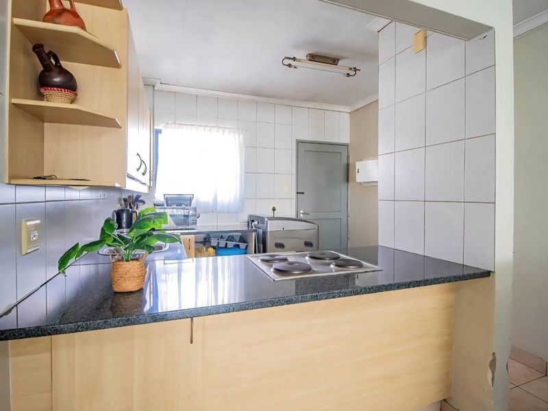 A functional kitchen featuring light wood cabinetry, granite countertops, an integrated electric hob, and tiled splashbacks, offering a practical layout for daily use.