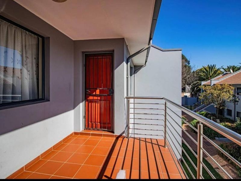 A clean, well-maintained balcony featuring terracotta-style floor tiles, a modern stainless steel balustrade, and a secure entrance door.