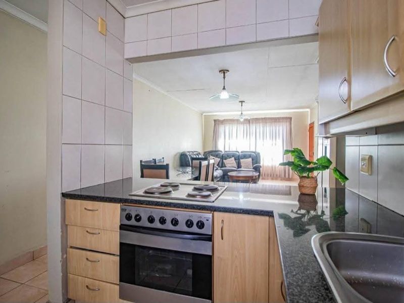 Open-plan kitchen featuring granite countertops, built-in oven and hob, and tiled backsplash, flowing into the adjacent living area.