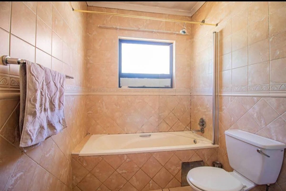 A functional bathroom featuring a built-in bathtub with a shower screen, toilet, and full-height wall tiling.