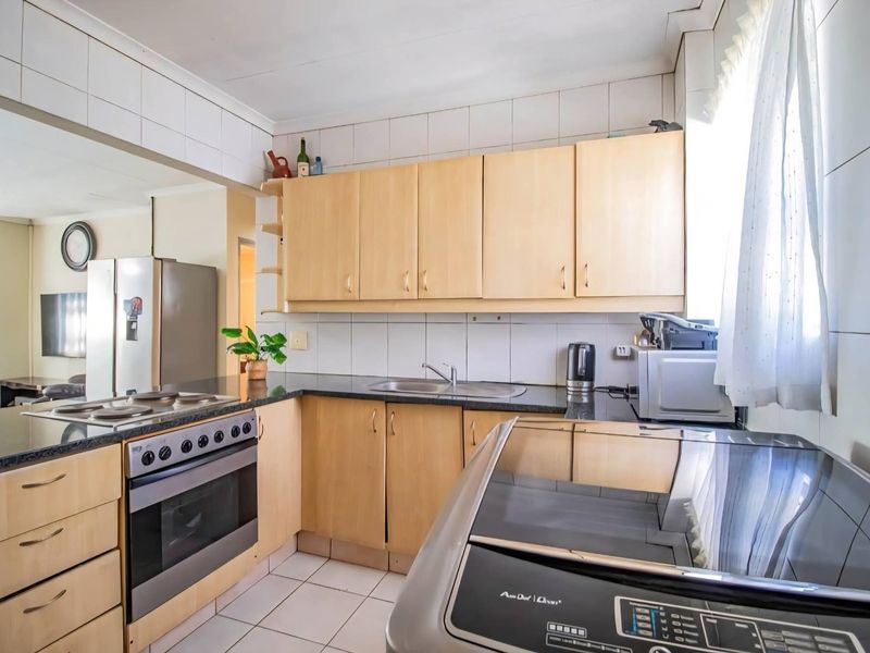 Functional kitchen featuring light wood cabinetry, granite countertops, built-in oven, and hob, with tiled walls and flooring throughout.