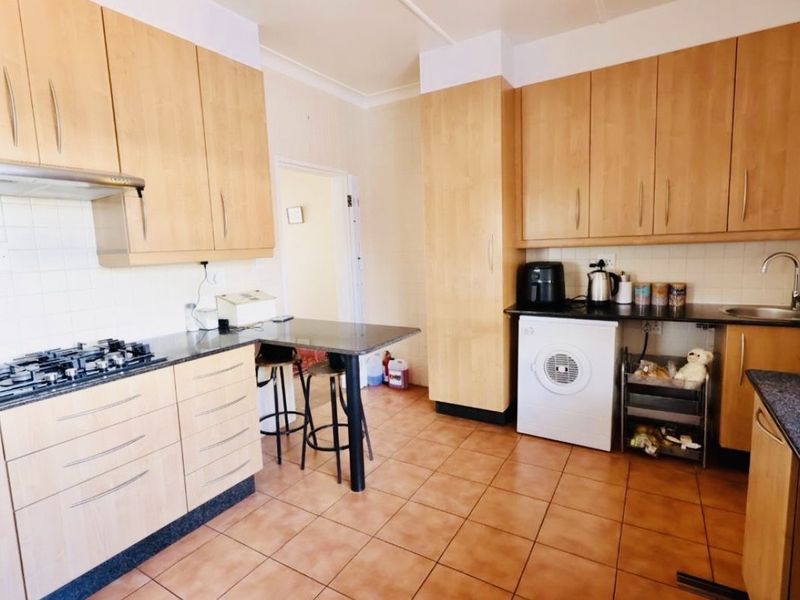A functional kitchen featuring light wood cabinetry, granite countertops, a gas hob with extractor, and tiled flooring with integrated laundry appliance space.