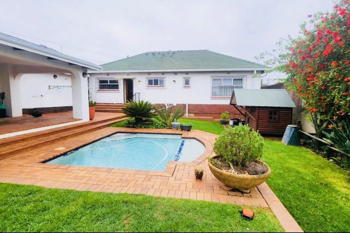 Rear exterior view featuring a swimming pool, covered patio area, and landscaped garden with brick paving and established greenery.