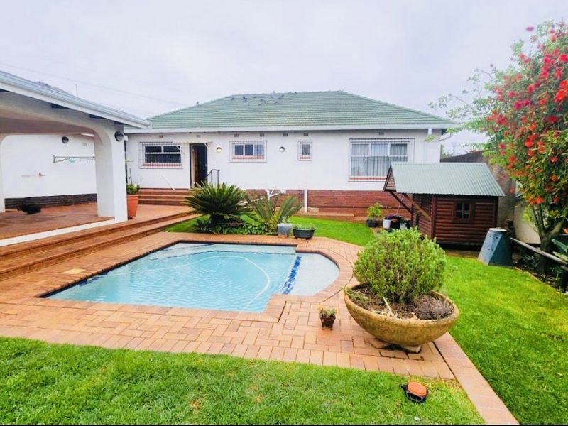 Rear exterior view featuring a swimming pool, covered patio area, and landscaped garden with brick paving and established greenery.