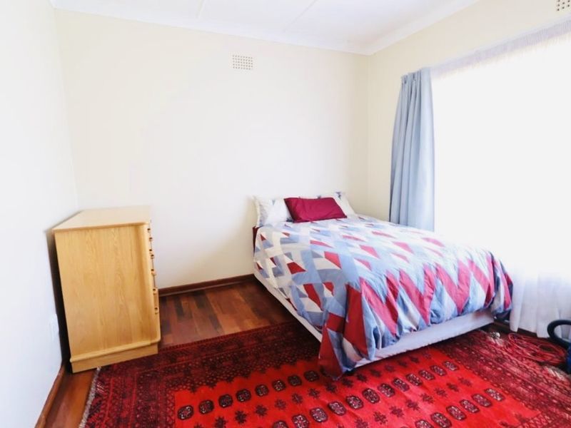 A bedroom featuring polished hardwood flooring, neutral wall finishes, and a ventilation grille, offering a clean and functional living space.