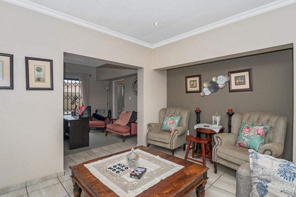 A comfortable living room featuring tiled flooring, crown molding, and recessed lighting, with an adjoining space visible through a wide opening.