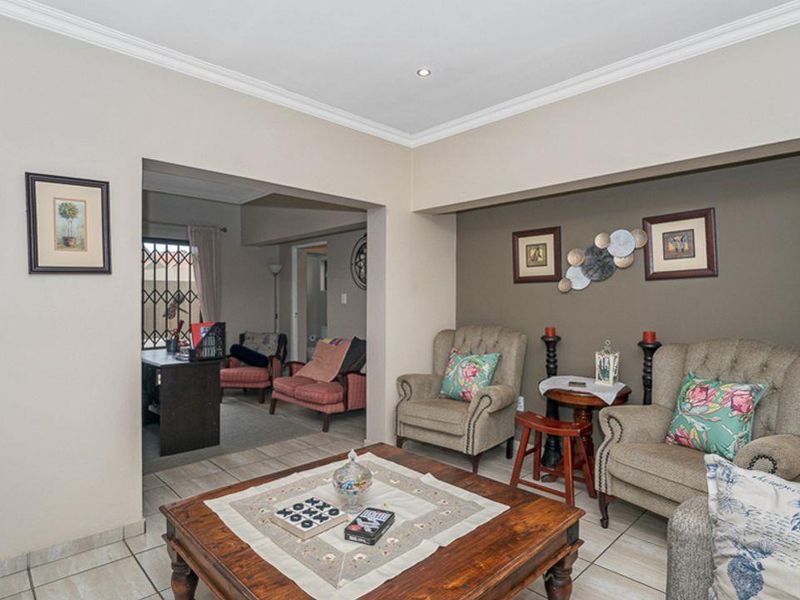 A comfortable living room featuring tiled flooring, crown molding, and recessed lighting, with an adjoining space visible through a wide opening.