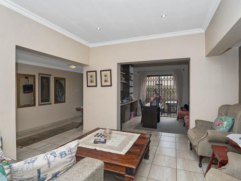 Spacious living area featuring neutral walls, tiled flooring, recessed lighting, and an adjoining study space with built-in shelving and security gate access.
