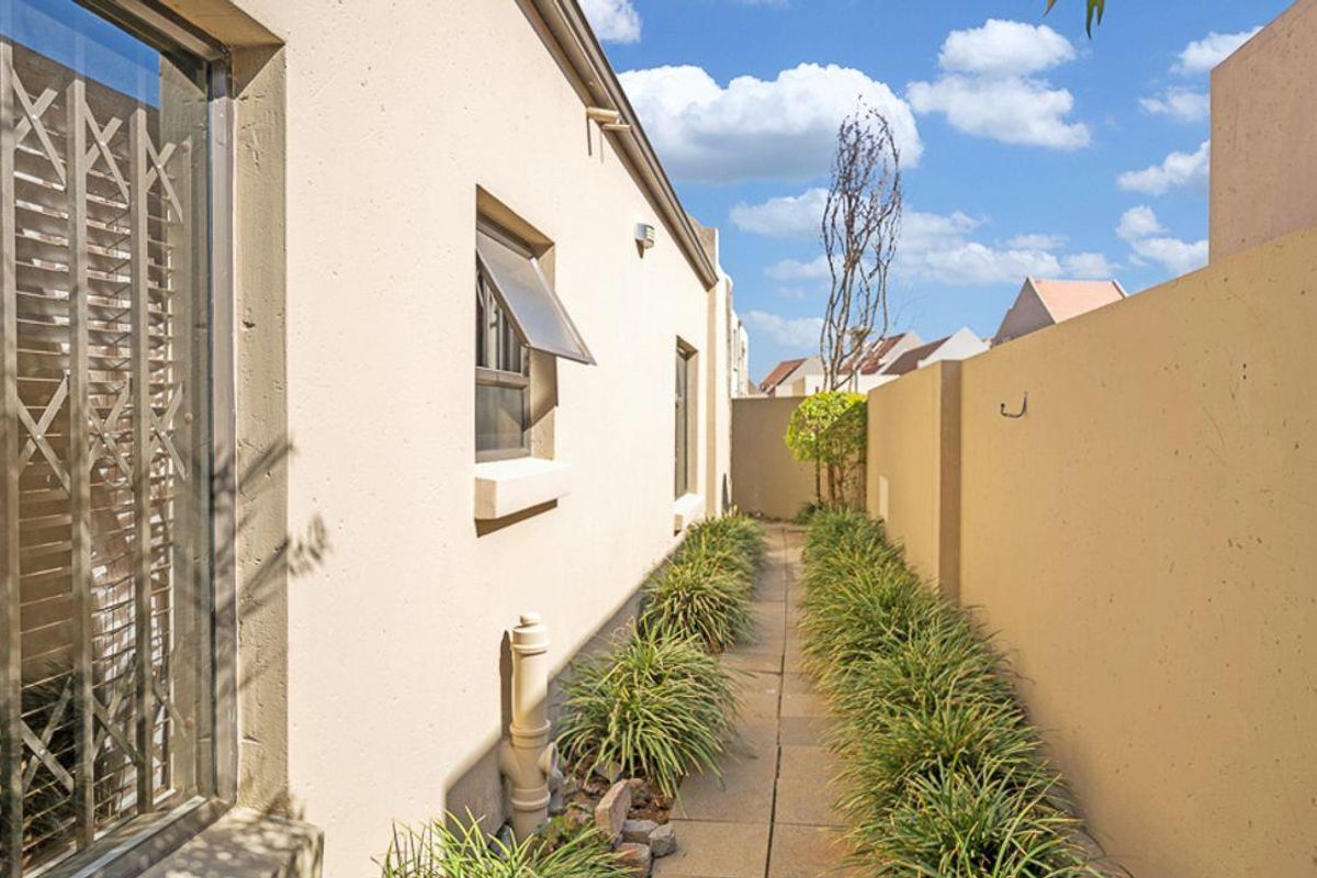 A narrow side passage featuring a paved walkway, boundary wall, and security gate access to the property.