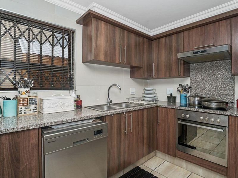 A functional kitchen featuring wood-finish cabinetry, granite countertops, integrated stainless steel appliances, and tiled flooring with security bars on the window.