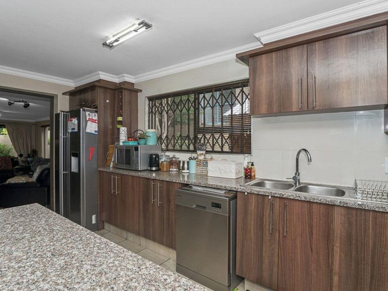 Functional kitchen featuring granite countertops, ample laminate cabinetry, and a double basin sink, with a view through to the adjacent living area.
