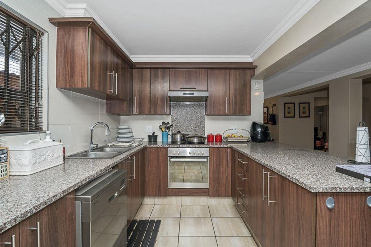 A functional kitchen featuring dark wood cabinetry, granite countertops, tiled flooring, and integrated appliances including an oven and extractor fan.