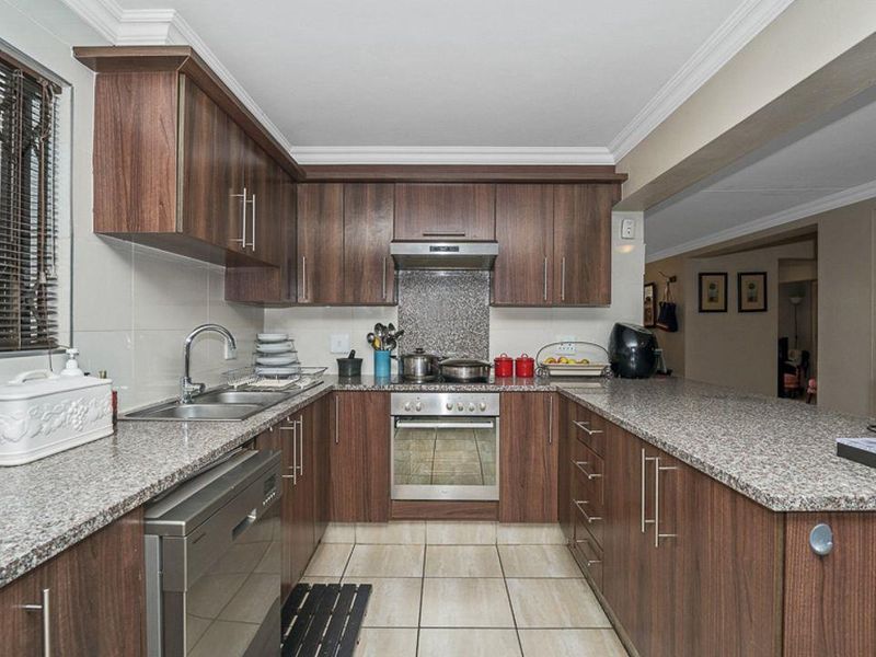 A functional kitchen featuring dark wood cabinetry, granite countertops, tiled flooring, and integrated appliances including an oven and extractor fan.
