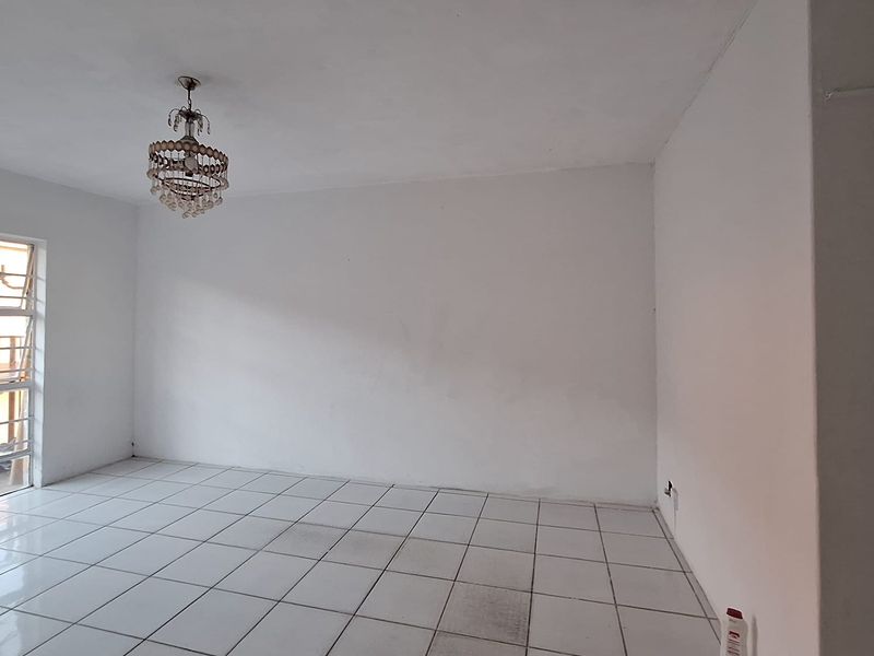 An empty living room featuring white ceramic floor tiles and a decorative crystal chandelier, offering a blank canvas for interior design.