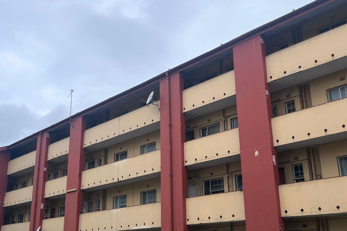 Exterior view of a multi-story apartment building featuring balconies and casement windows, showing signs of exterior wear and weathering.