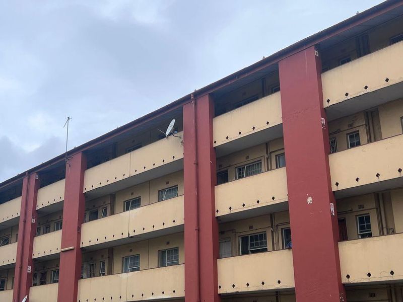 Exterior view of a multi-story apartment building featuring balconies and casement windows, showing signs of exterior wear and weathering.