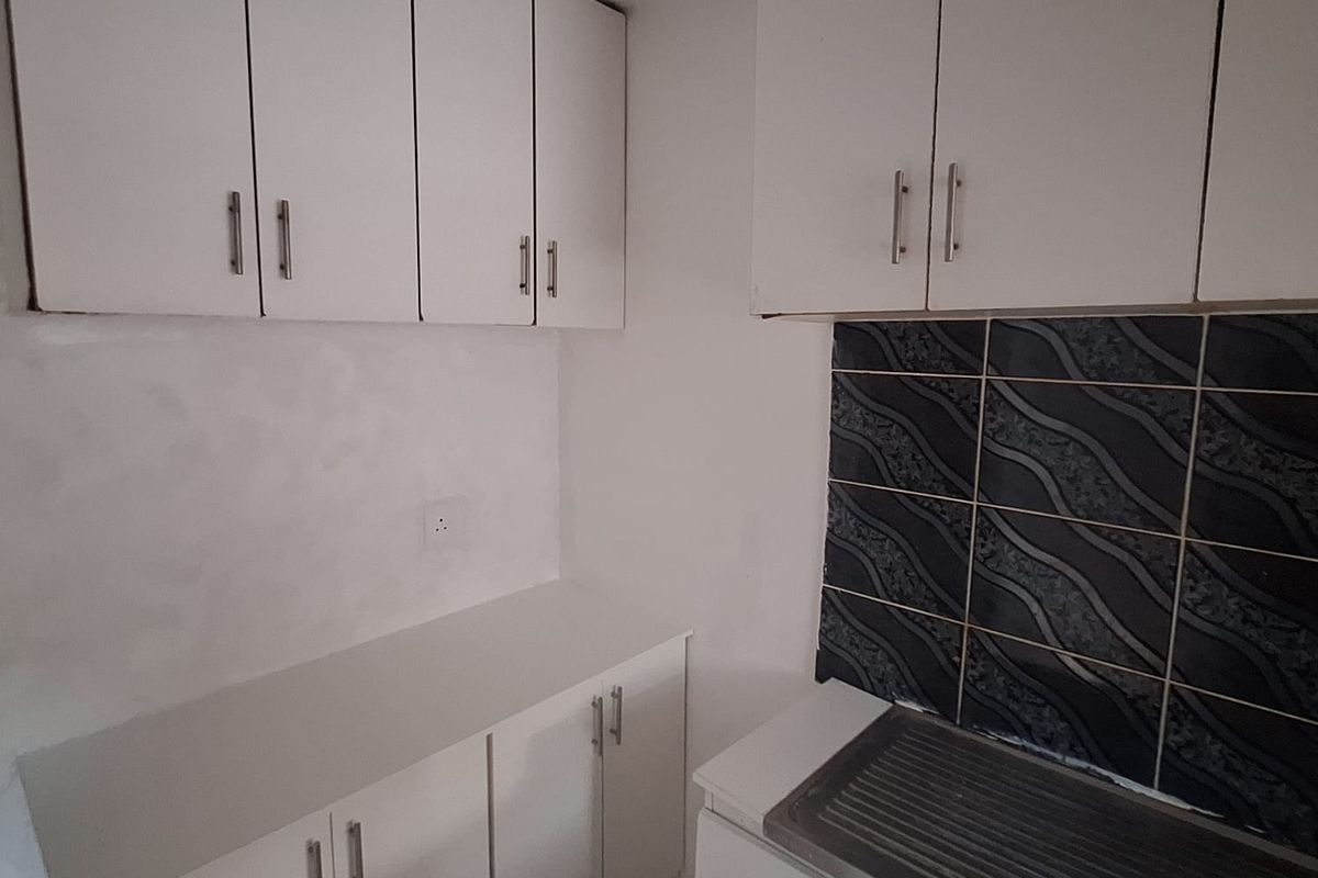 A compact kitchen featuring white built-in cabinetry, a stainless steel sink, and a decorative tiled backsplash.