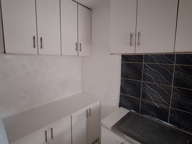 A compact kitchen featuring white built-in cabinetry, a stainless steel sink, and a decorative tiled backsplash.