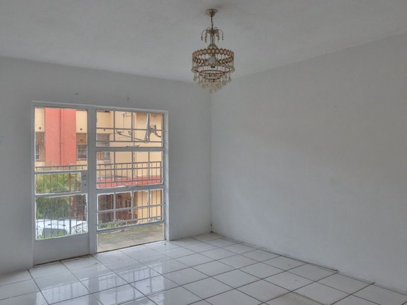 An empty living room featuring white tiled flooring, a decorative chandelier, and a glass door providing natural light and exterior access.