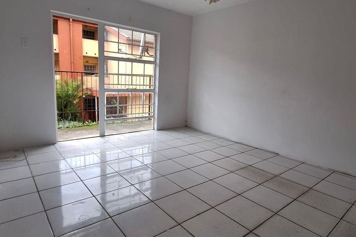An empty living room featuring white tiled flooring and a large window with security bars, offering a blank canvas for potential interior design.