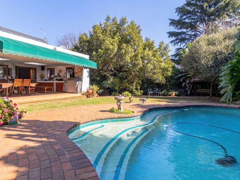 A well-maintained outdoor entertainment area featuring a swimming pool, brick-paved surround, and a covered patio with a retractable awning.