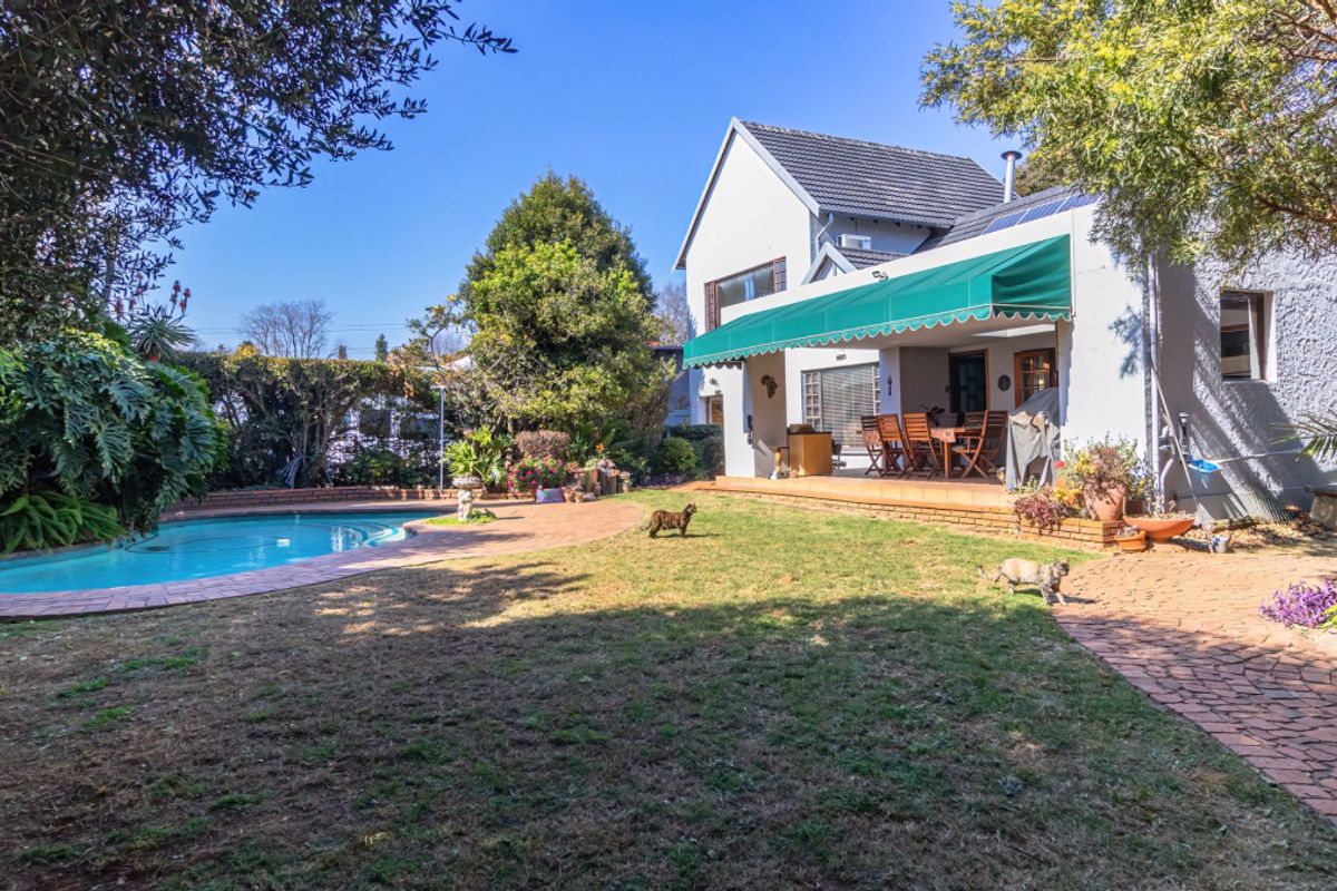 Rear view of the property featuring a swimming pool, a paved patio area with a retractable awning, and a well-maintained garden.