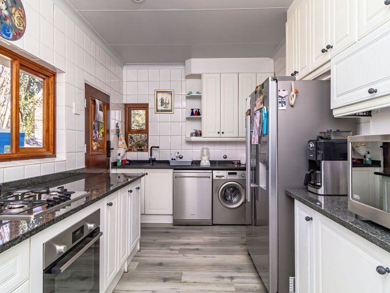 A functional kitchen featuring white cabinetry, granite countertops, a gas hob, built-in oven, and integrated laundry appliances with tiled splashbacks and laminate flooring.