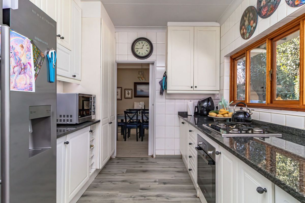 A functional kitchen featuring white cabinetry, granite countertops, a built-in oven, and a gas hob, with a view through to the dining area.