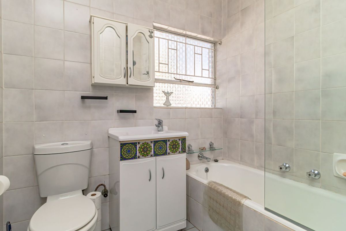 A functional bathroom featuring a bathtub with a glass screen, a built-in vanity unit, and full-height wall tiling.