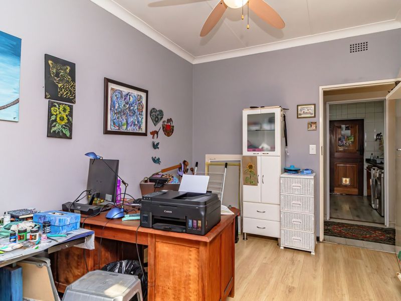 A functional home office space featuring laminate flooring, coving, and a ceiling fan, with direct access to an adjacent utility area.