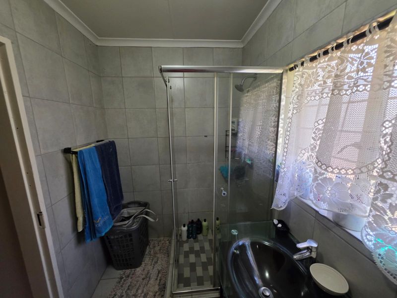 A functional bathroom featuring a glass shower enclosure, tiled walls, and a modern vanity basin with a mixer tap.